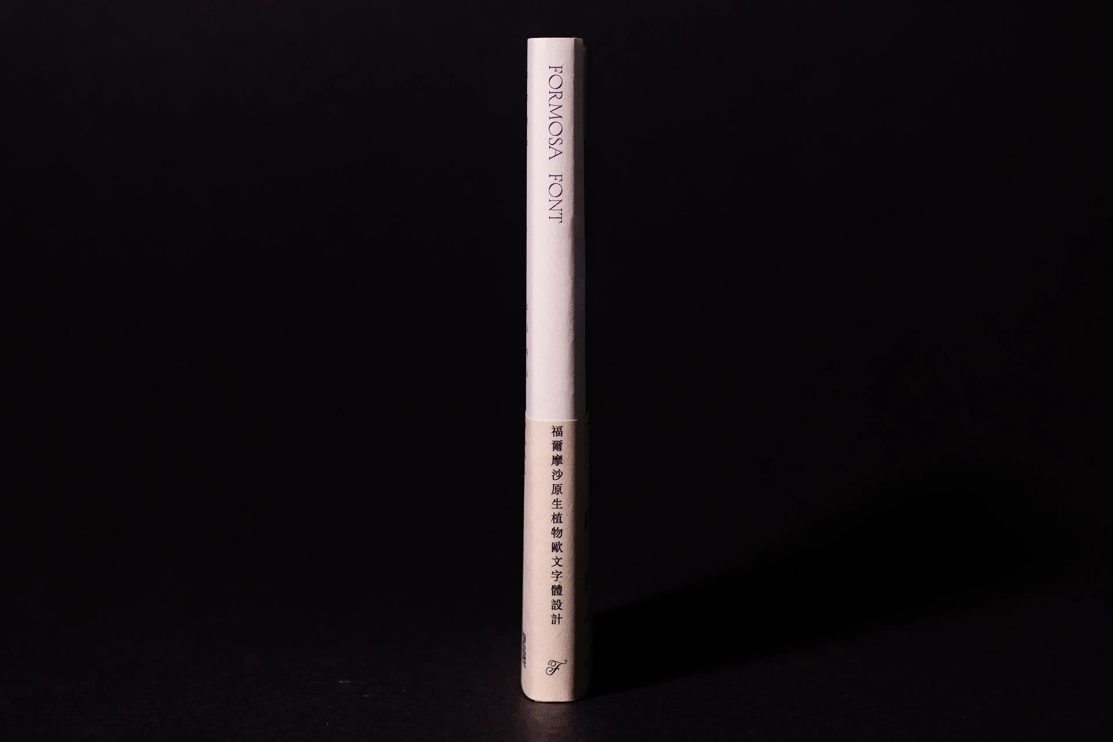The spine of the Formosa Font book stands upright against a dark background, showing the title "FORMOSA FONT" in Latin letters at the top and vertical Chinese text below. The minimal white cover contrasts sharply with the black backdrop, highlighting the clean typographic layout.