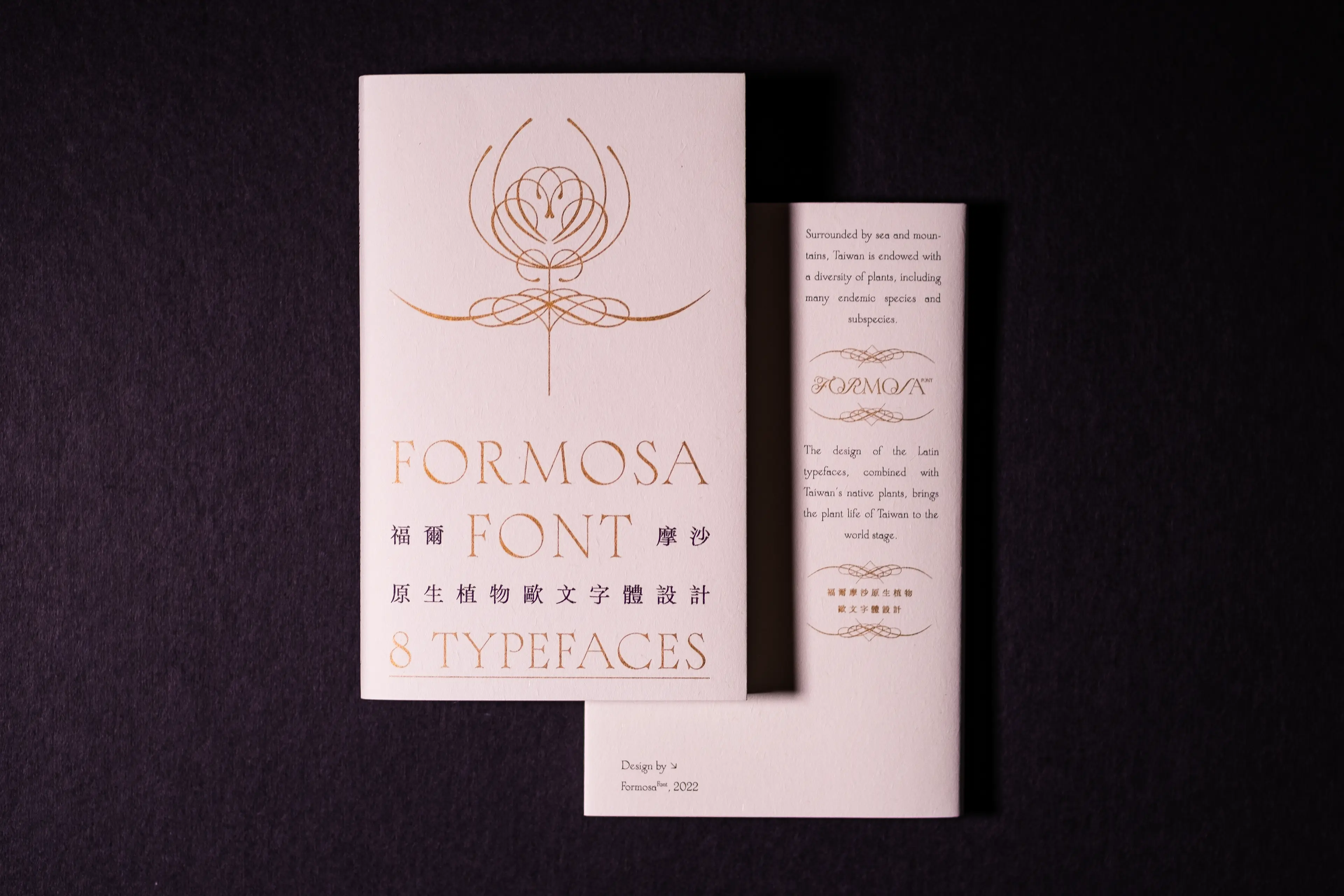 A cream-colored booklet for Formosa Font displayed front and back against a dark background, featuring elegant gold foil typography that blends Latin letterforms with Chinese characters and a delicate botanical line illustration on the cover.