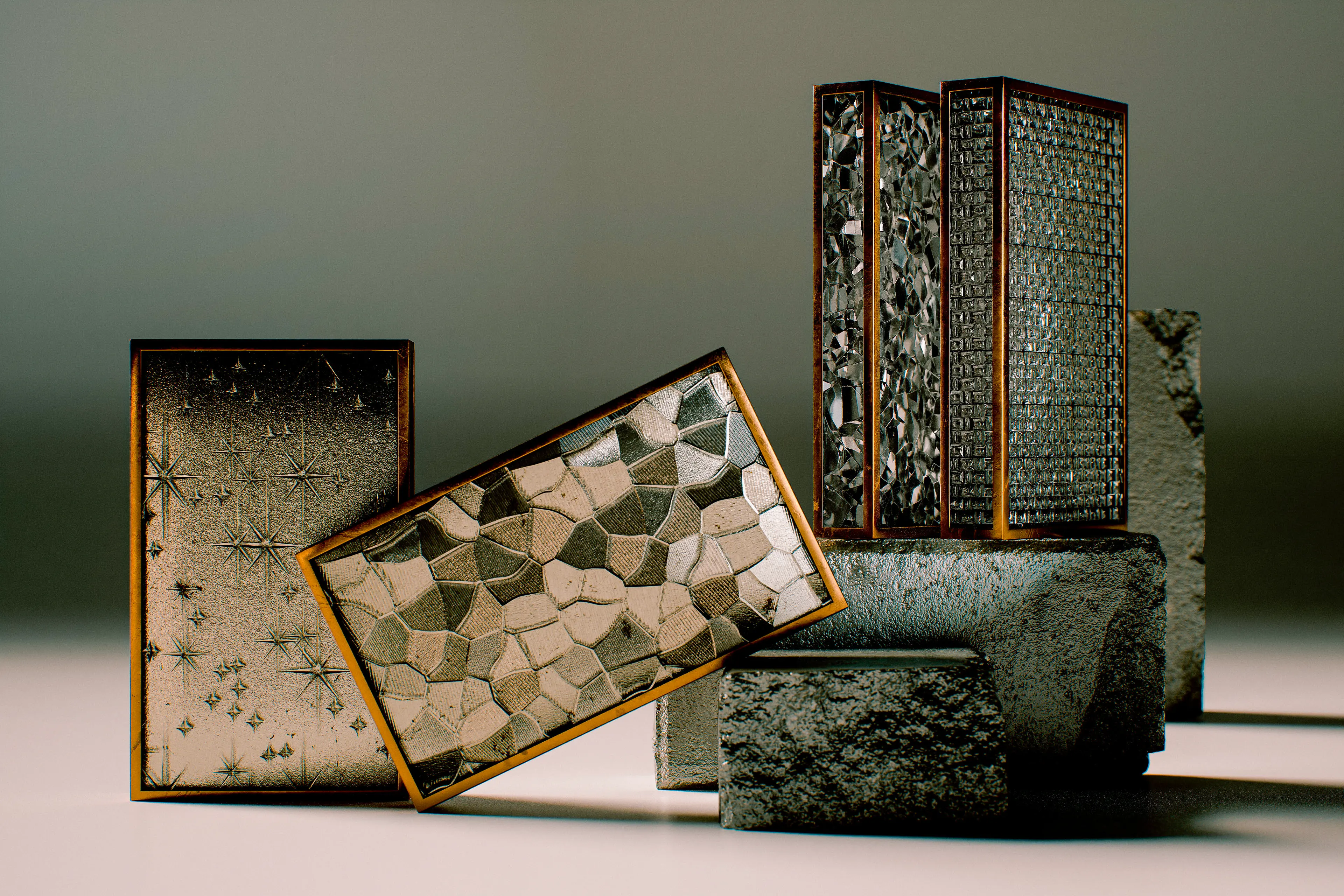 A collection of handcrafted notebooks and boxes with wood-framed covers featuring textured patterned glass surfaces — including geometric mosaic, star-etched, and rippled or crackled glass designs — arranged in a moody studio still life alongside rough stone props.