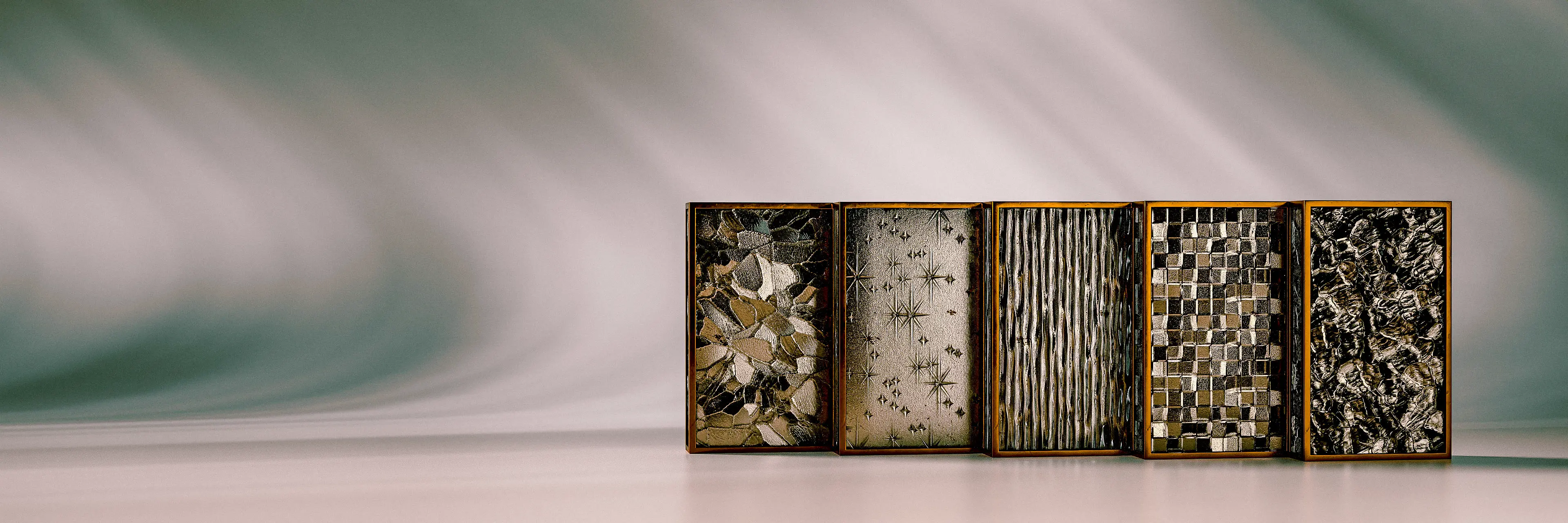Five small framed panels stand side by side against a softly draped grey-green backdrop, each displaying a distinct patterned glass texture — from floral and star motifs to vertical ribbing, a grid mosaic, and shattered fragments — all set in warm gold-toned wooden frames.