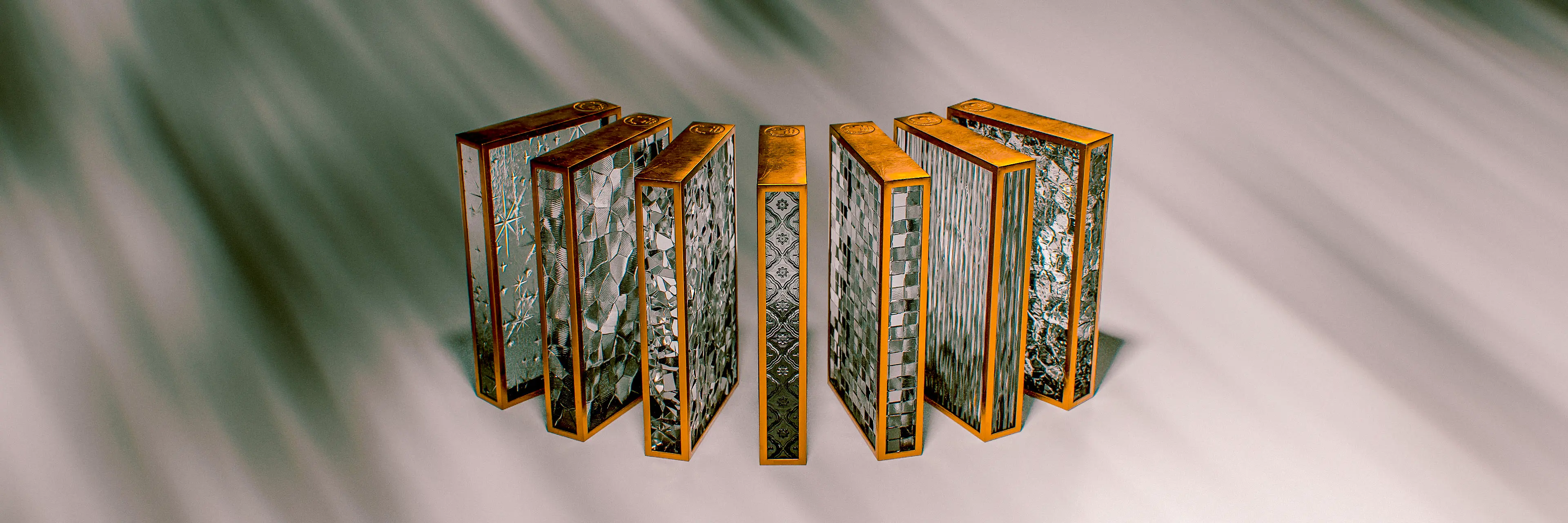 Four notebooks fanned open and arranged symmetrically, showcasing covers with a dark marbled glass texture framed in gold, with one spine featuring an intricate blue geometric tile pattern, all set against a soft grey draped background.