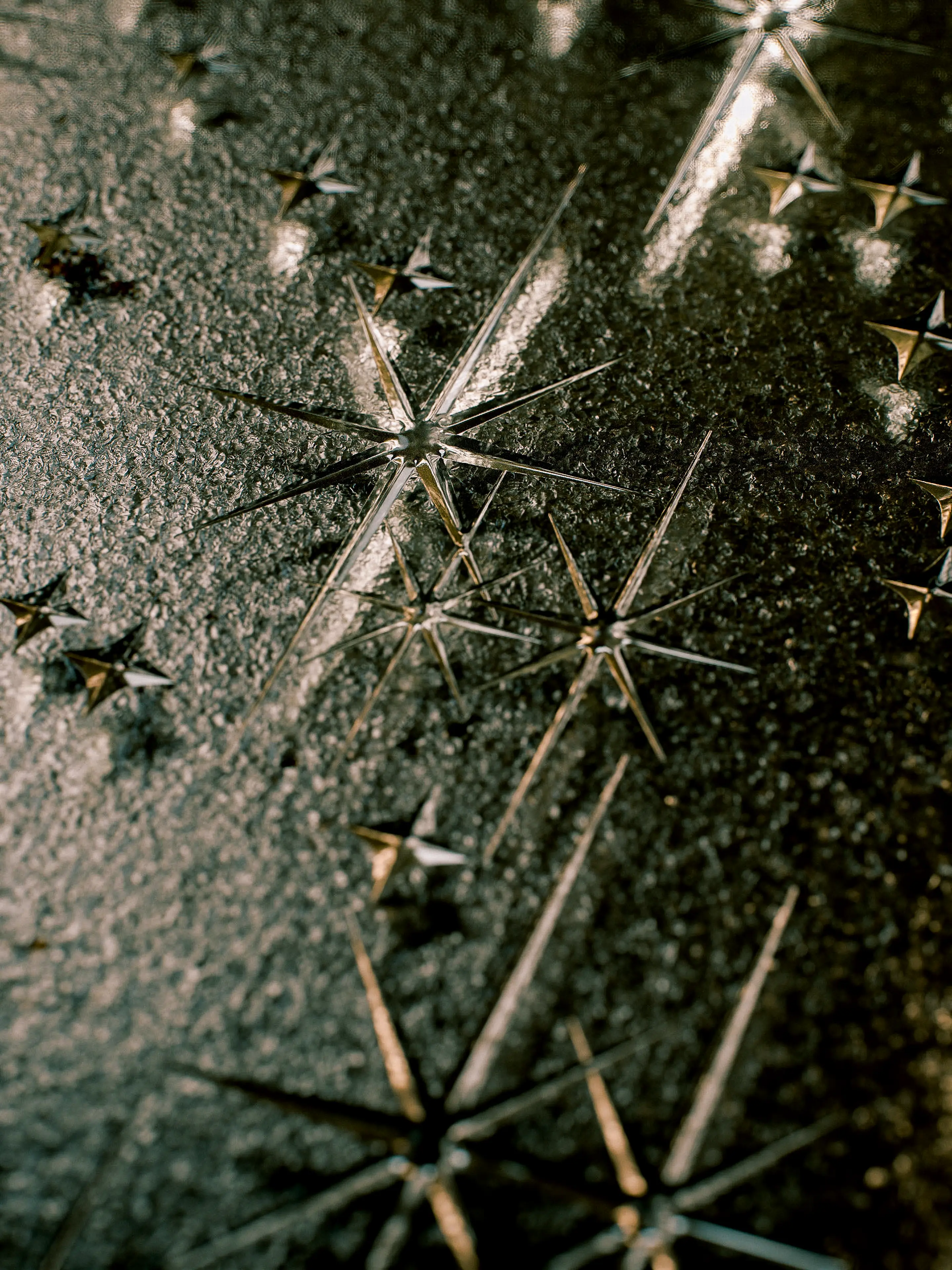 Close-up of a dark textured notebook cover featuring an embossed geometric pattern of sharp, multi-pointed star motifs connected by fine diagonal lines, rendered in a metallic silver finish against a deep charcoal surface.